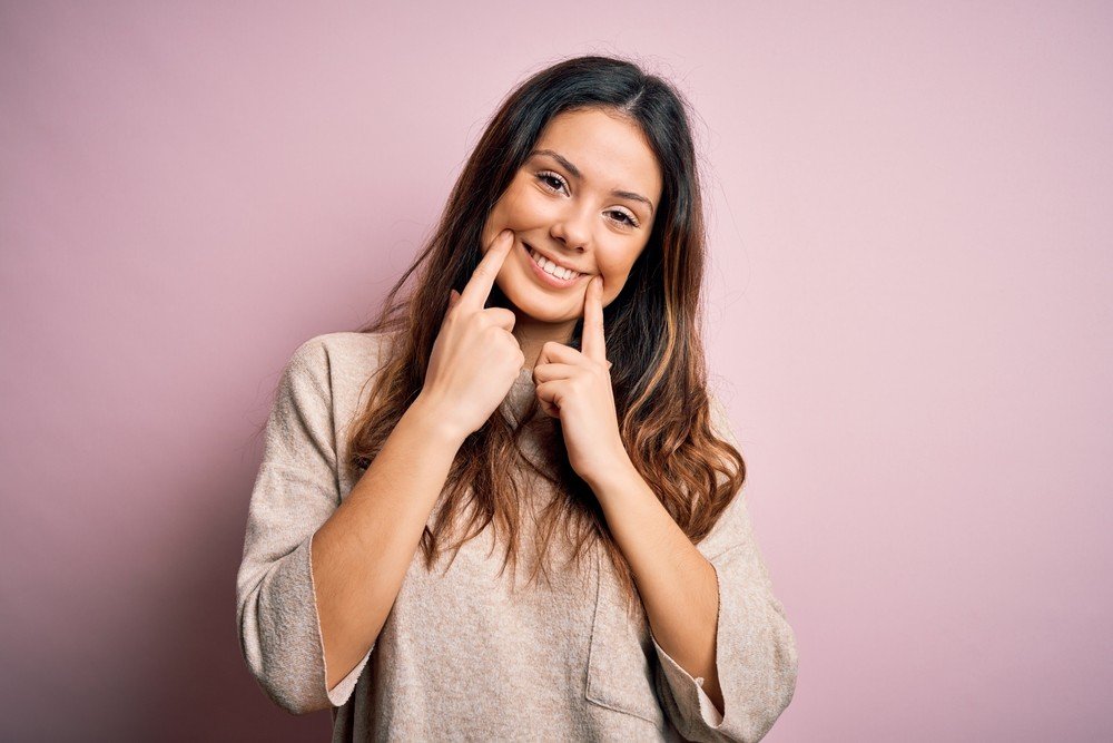Mujer sonriendo y señalando su sonrisa